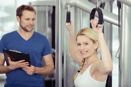 Happy Pretty Woman Exercising at the Fitness Gym with Male Instructor.