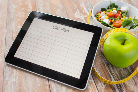 healthy eating, dieting and weigh loss concept - close up of diet plan on tablet pc screen, green apple, measuring tape and sald